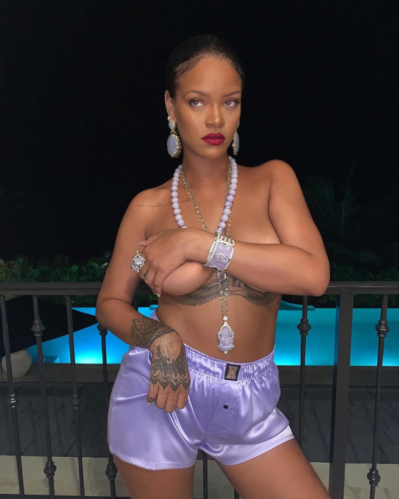 A topless Rihanna posing by a pool.