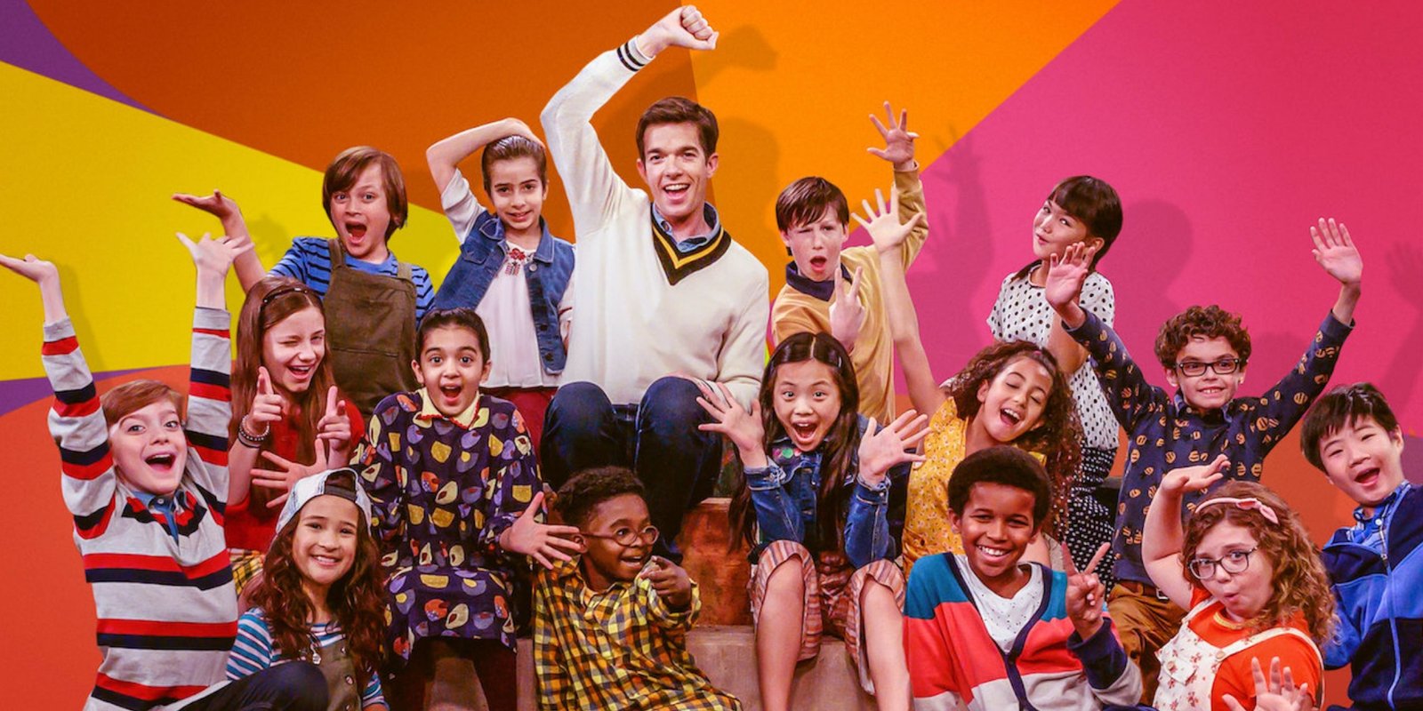 John Mulaney and a group of kids grinning in front of a multicolored background in John Mulaney & The Sack Lunch Bunch